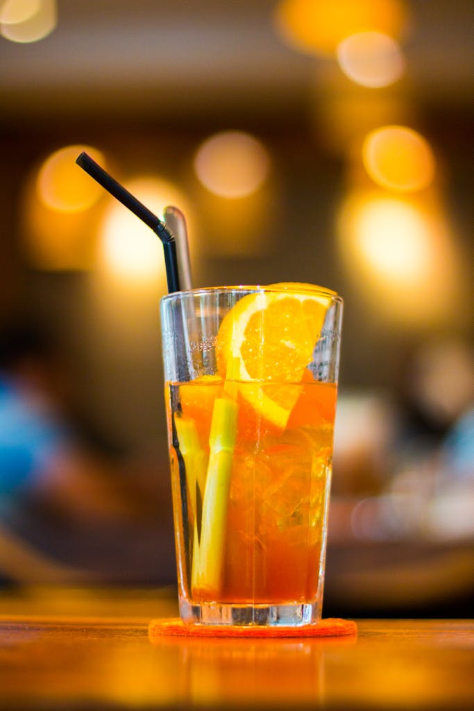 Close-up of a refreshing orange cocktail with lemon slices and straw, perfect for summer vibes.